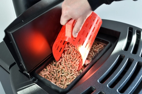 Eine Hand füllt mit einer Schaufel eine Pellet-Heizung mit Pellets.